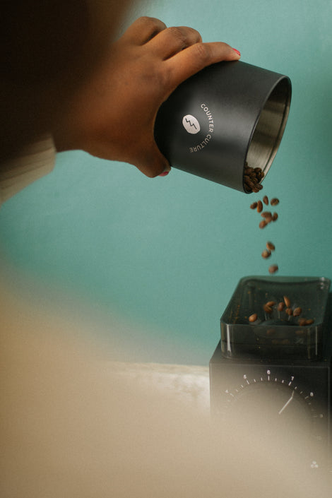 Photo of a person pouring coffee beans into a coffee grinder.