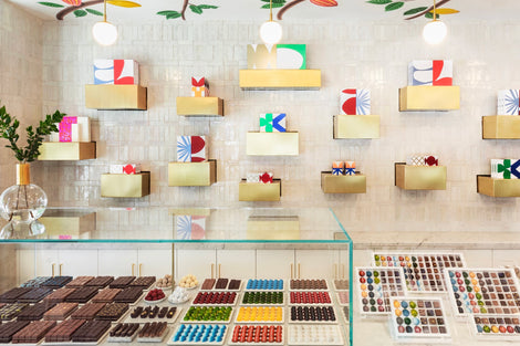 Photo of the interior of andSons chocolate shop. There is a large case with chocolates on a counter and on the wall are various sized boxes.