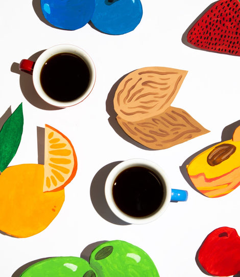 Top down photo of two cups of coffee surrounded by hand made cut outs of different fruits. 