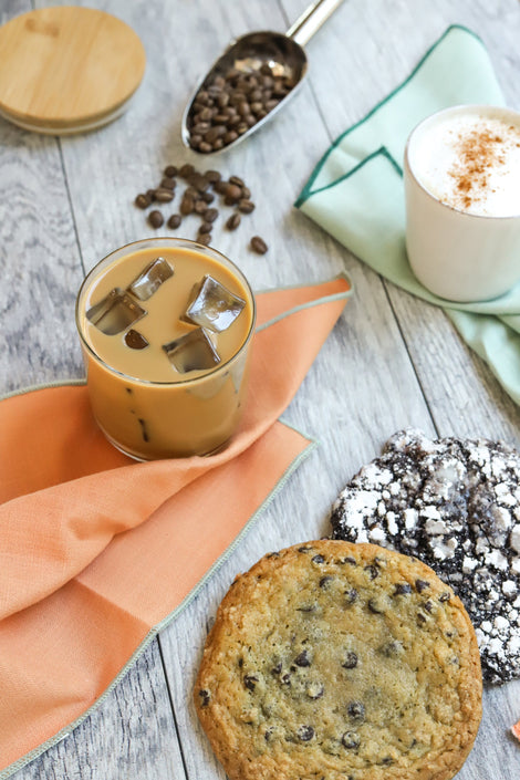 Photo of two coffee drinks on napkins next to cookies.