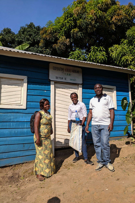 Three members of the Muungano Cooperative standing outside of a building and smiling at the camera.