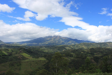 Photo of green rolling hills with a mountain in the background surrounded by clouds.